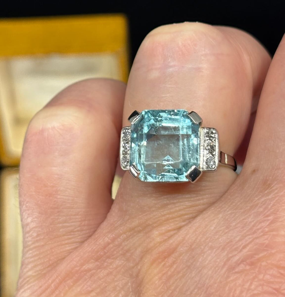 Four claw aquamarine and diamond ring featured on the finger.