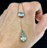 Edwardian aquamarine pendant necklace worn on hand featuring light blue pear and emerald cut aquamarines in 9ct yellow gold