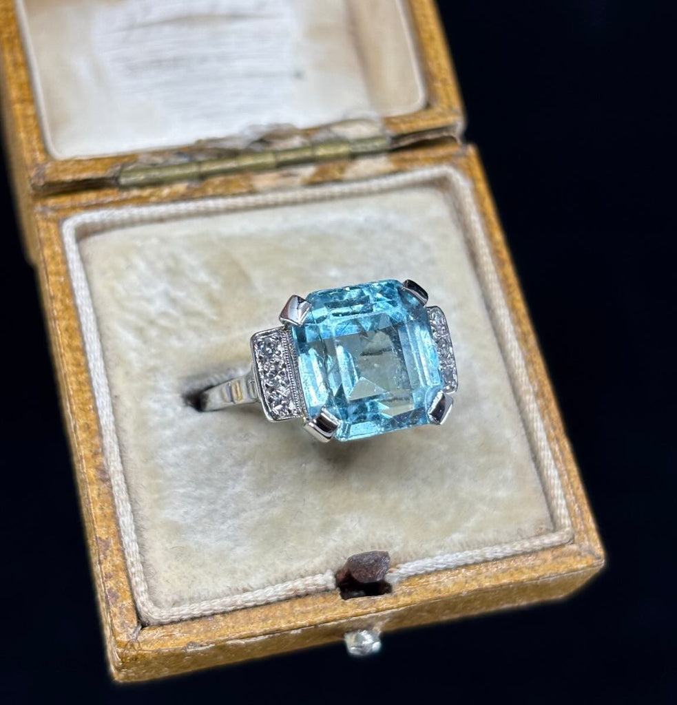 Close-up of 8.70ct emerald-cut aquamarine with diamond shoulders (0.12ct total) on a tapered 2.5–1.6mm 18ct white gold band.