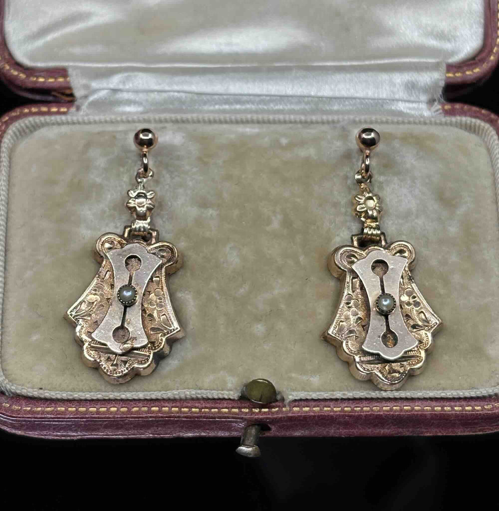 Angled view of Victorian 9ct rose gold earrings with floral engraved detailing and natural seed pearl accents.