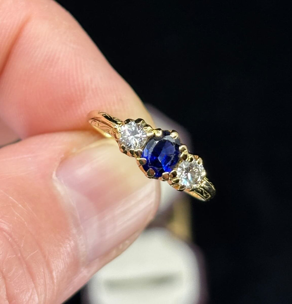 Mid‑century 1950s three‑stone ring photographed in a vintage box, highlighting the balanced oval sapphire and two round brilliant diamonds on a slim gold band.