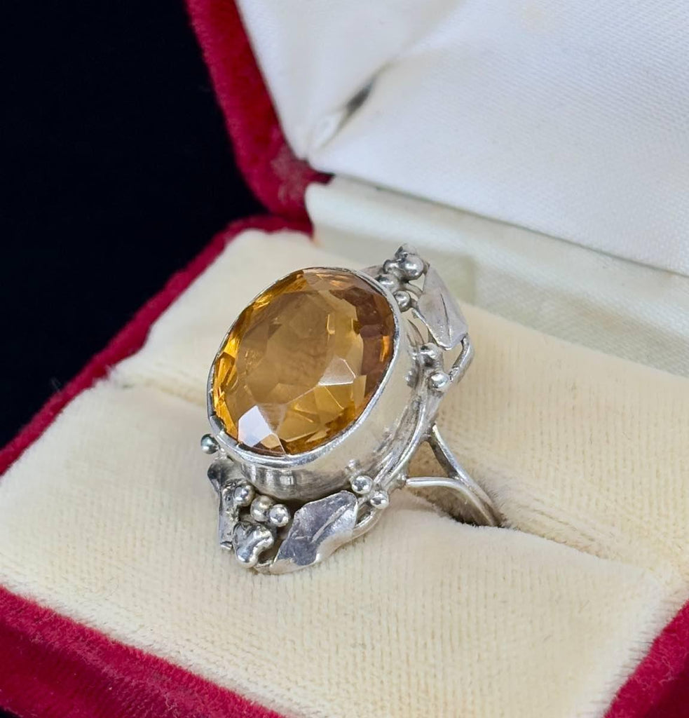 The large citrine stone is bezel set in silver and surrounded by gum leaves and gum nuts that are clustered at the top and bottom of the ring design.
