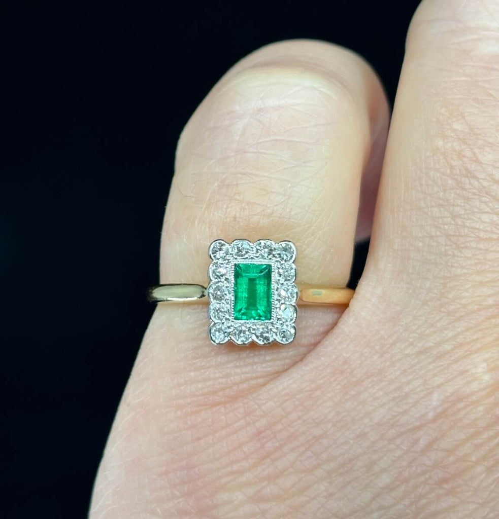 Art deco rectangular emerald cluster ring with a border of diamonds on the finger.