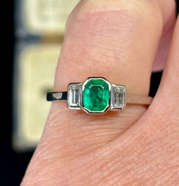 Bezel set emerald ring featuring a vivid Colombian emerald and baguette cut diamond shoulders on a slim 1.5mm 18ct white gold band, ideal for vintage jewellery lovers.