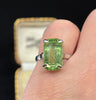 vintage green emerald cut peridot ring in white gold shown worn on the finger with a stunning elongated emerald cut peridot