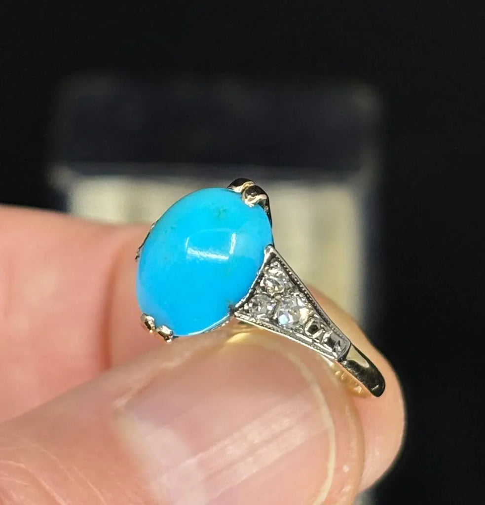  Detailed view of an Art Deco vintage ring featuring an oval turquoise center piece surrounded by sparkling diamond accents on the shoulders.