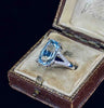 A cushion cut aquamarine four claw set in white gold with diamond accents, photographed in a side view in a ring box.