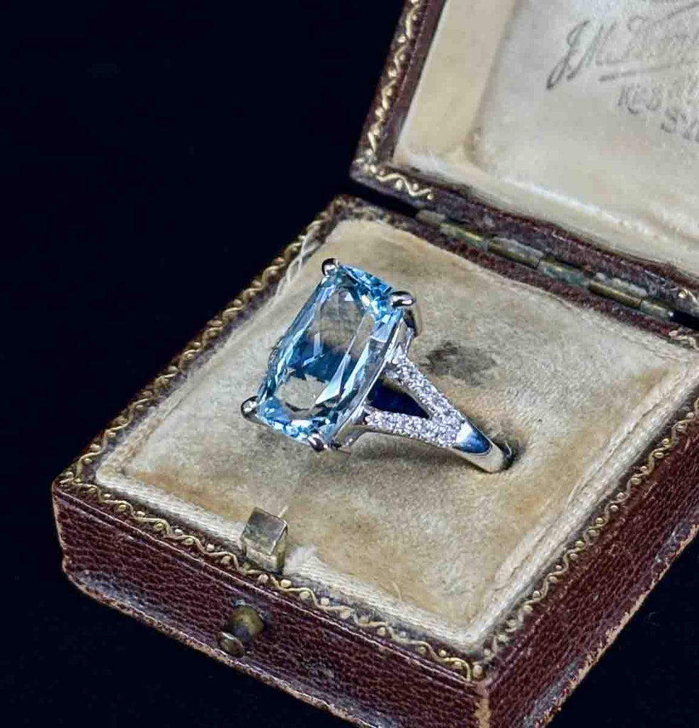 A cushion cut aquamarine four claw set in white gold with diamond accents, photographed in a side view in a ring box.