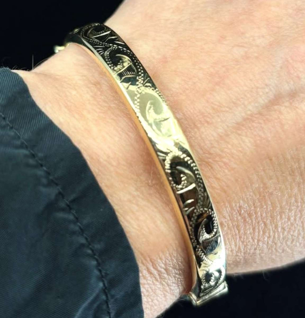 Contemporary 9ct yellow gold hand-engraved hinged bangle worn on wrist.